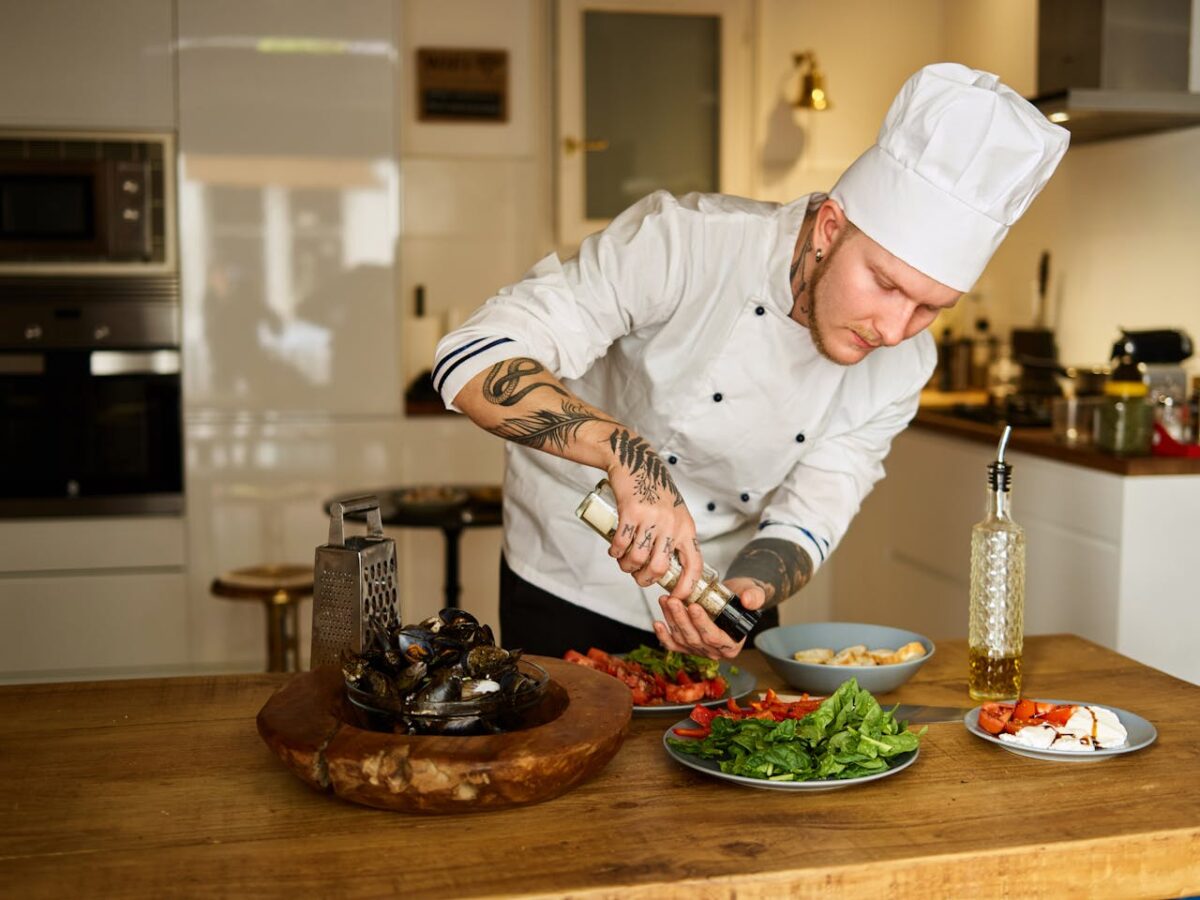 Chef in uniform seasoning fresh vegetables in a modern kitchen. Culinary arts and food preparation.